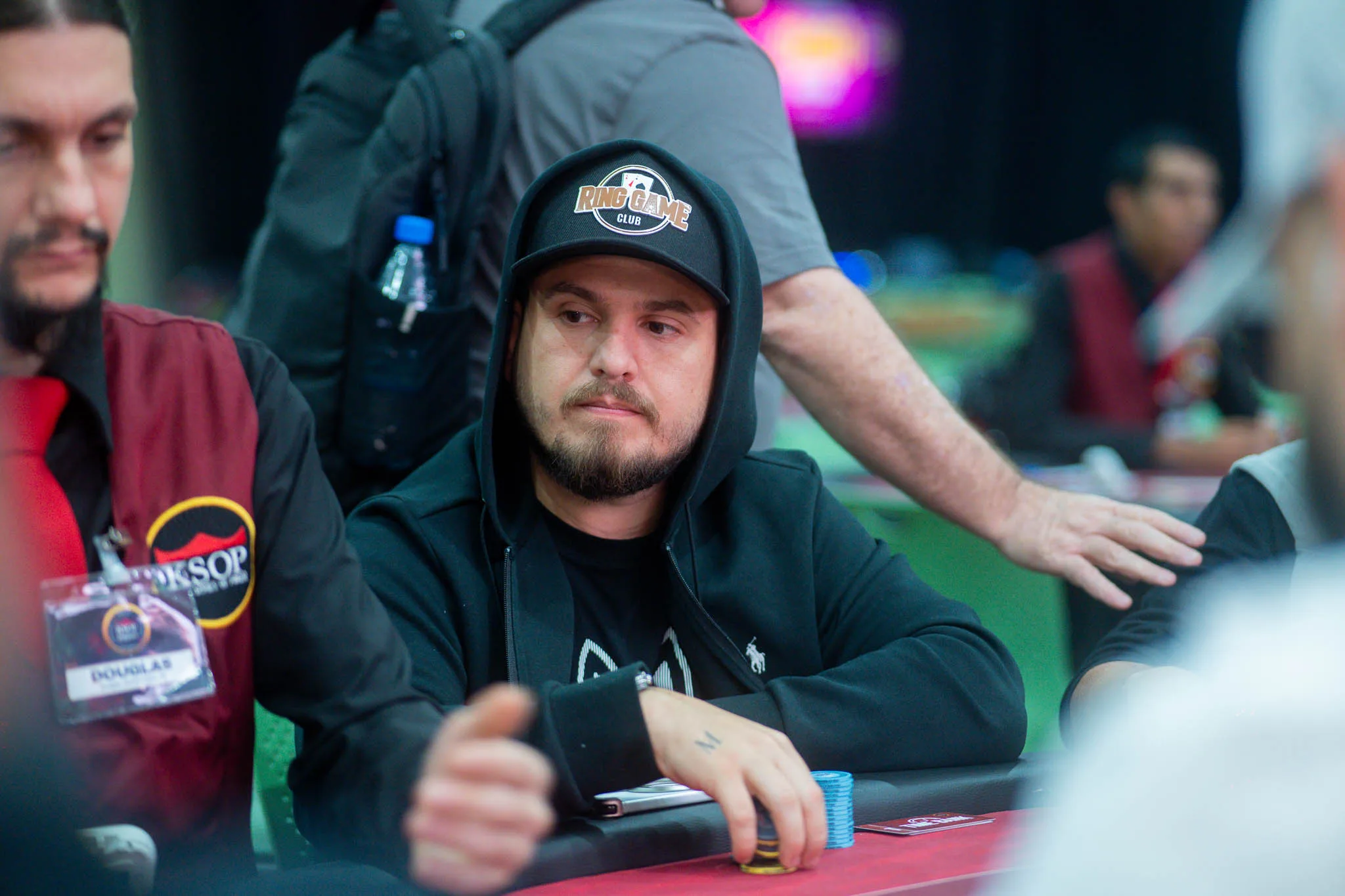 Poker chips and cards on a poker table with players in the background at a tournament