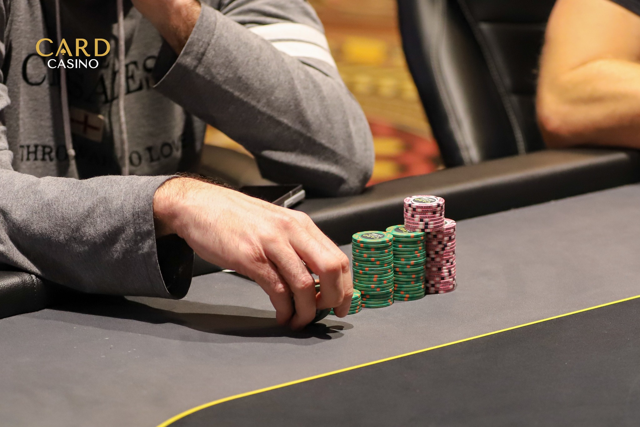 A close-up of a stack of poker chips on a green felt poker table, with a blurred background of a casino environment.