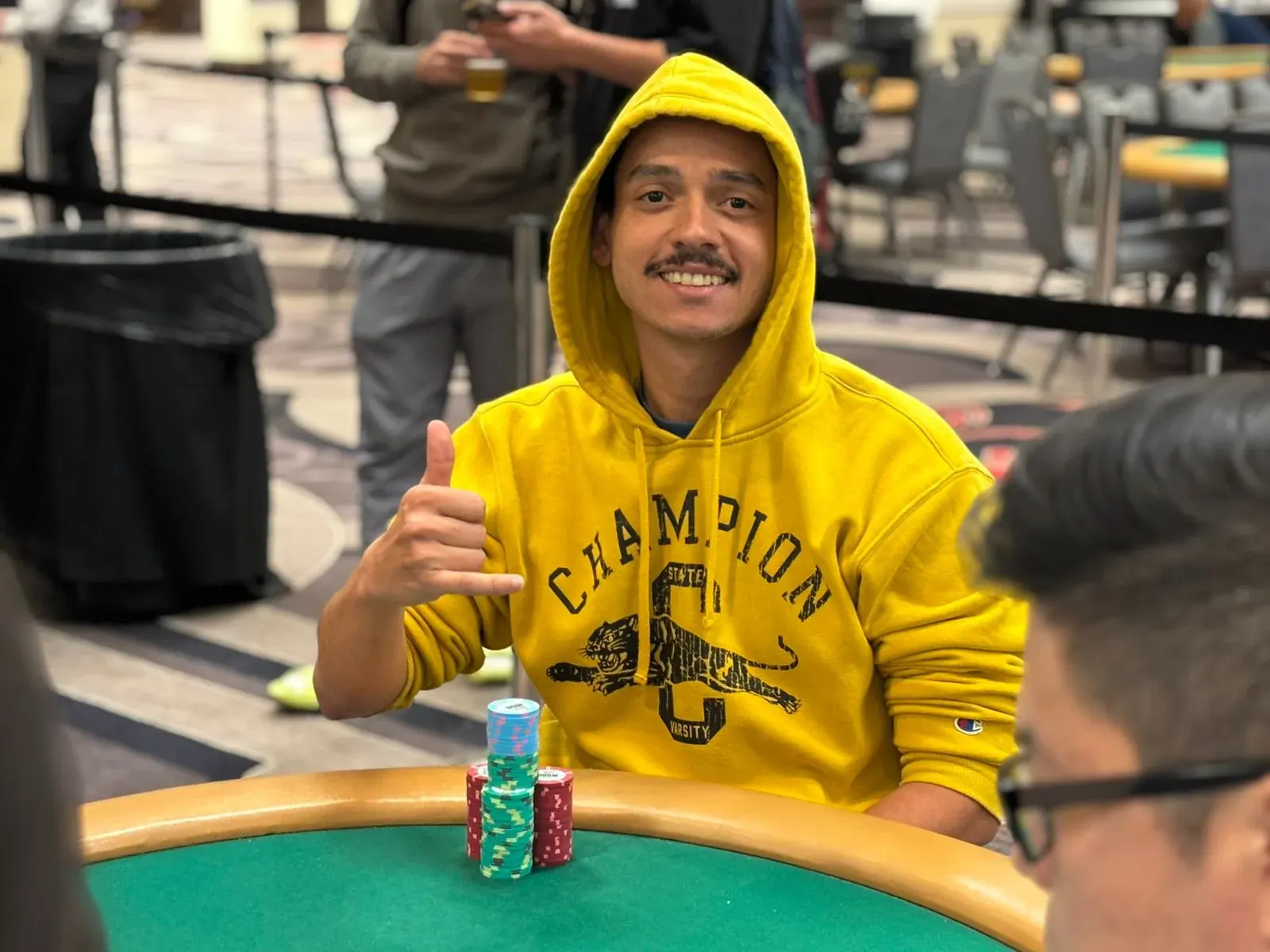 A group of diverse poker players are seated around a poker table during a tournament, with chips and cards visible.