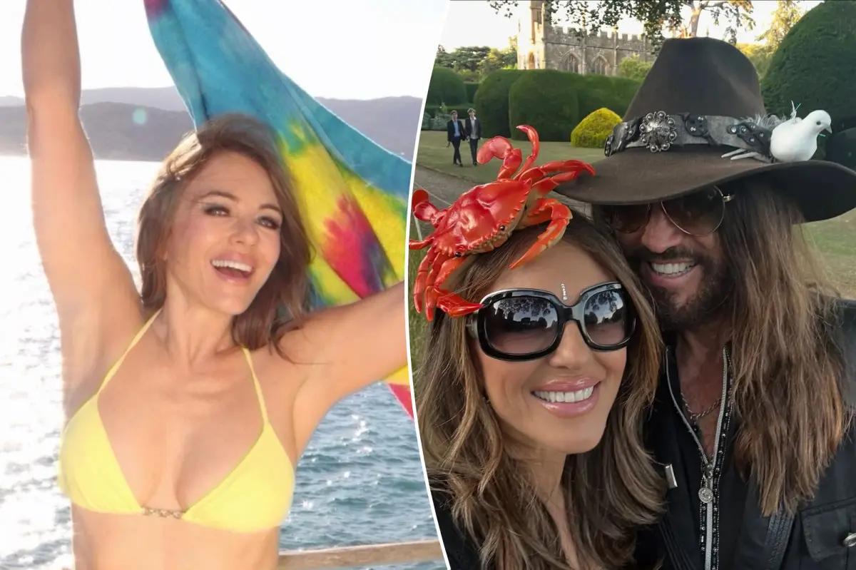 Elizabeth Hurley smiling on a beach, wearing a yellow bikini and holding a tie-dye flag.