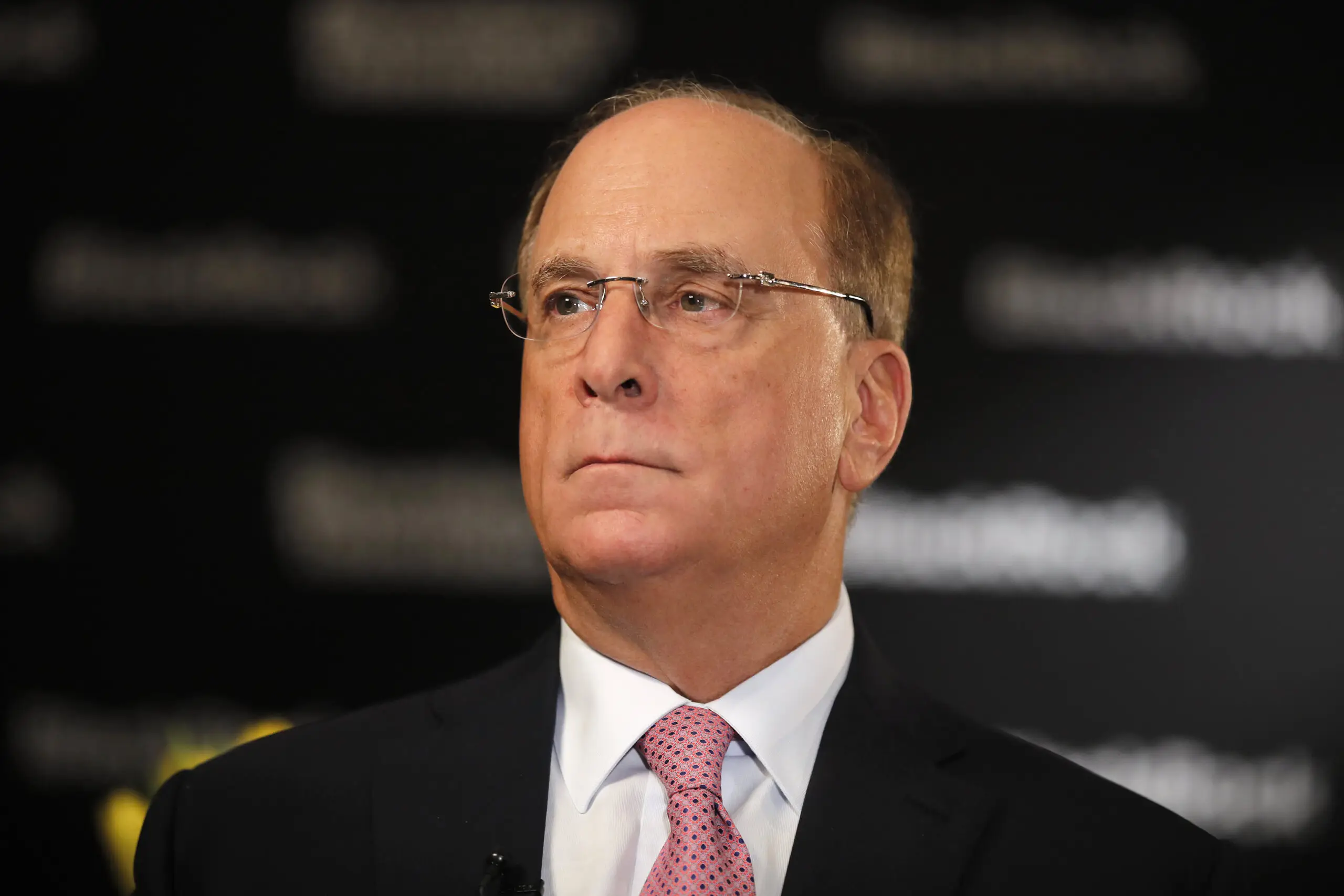 BlackRock CEO Larry Fink speaking with a microphone at a financial event.