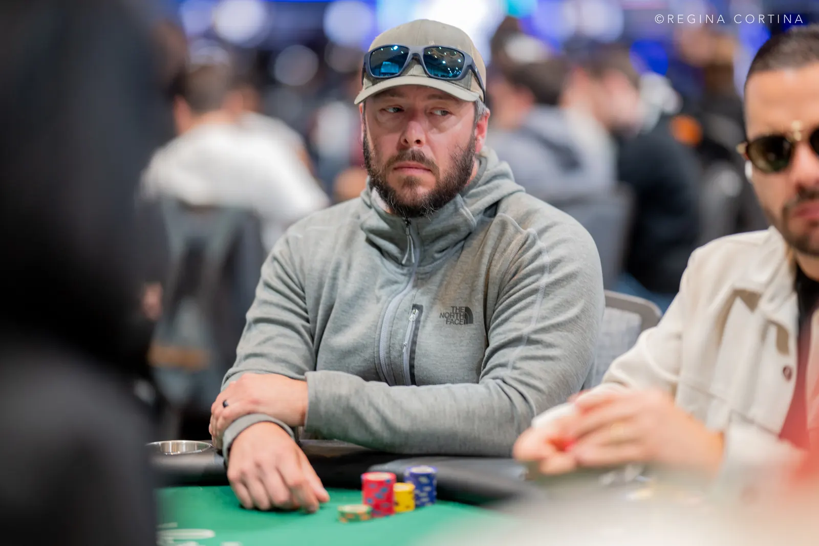 A poker player deep in thought at a World Series of Poker Main Event table, with other players and tournament officials observing.