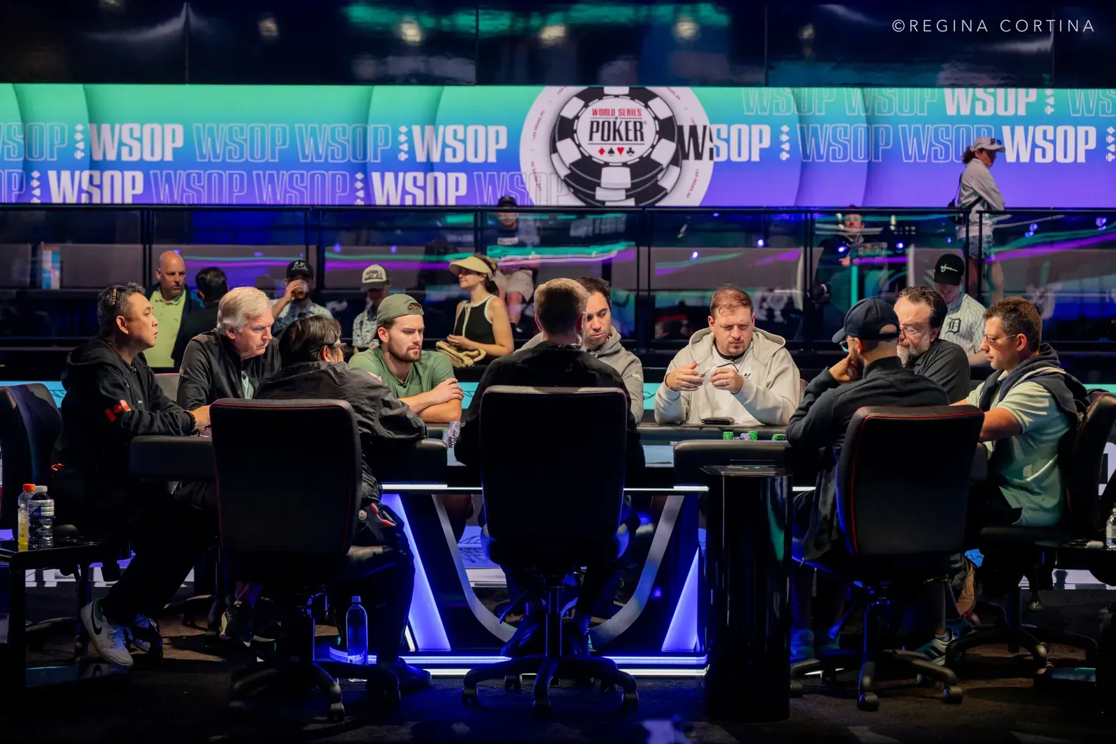 Players seated at a poker table during the World Series of Poker Main Event, with tournament officials observing.
