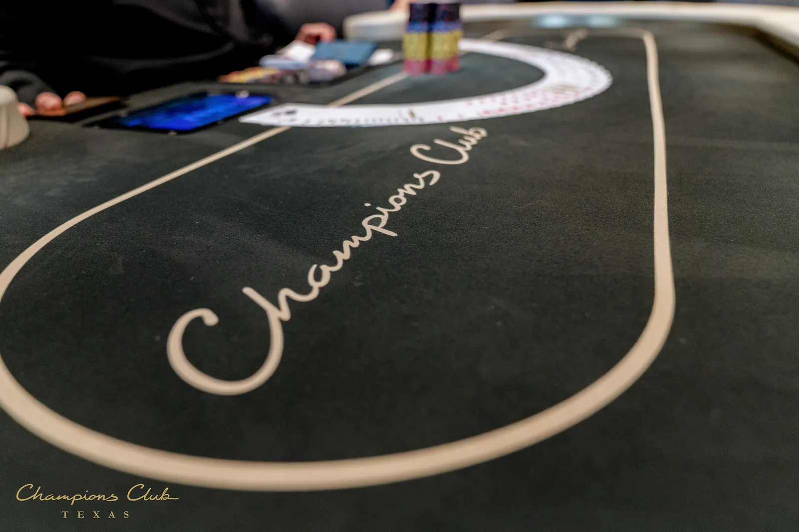 A group of poker players seated at a tournament table, with chips and cards visible.