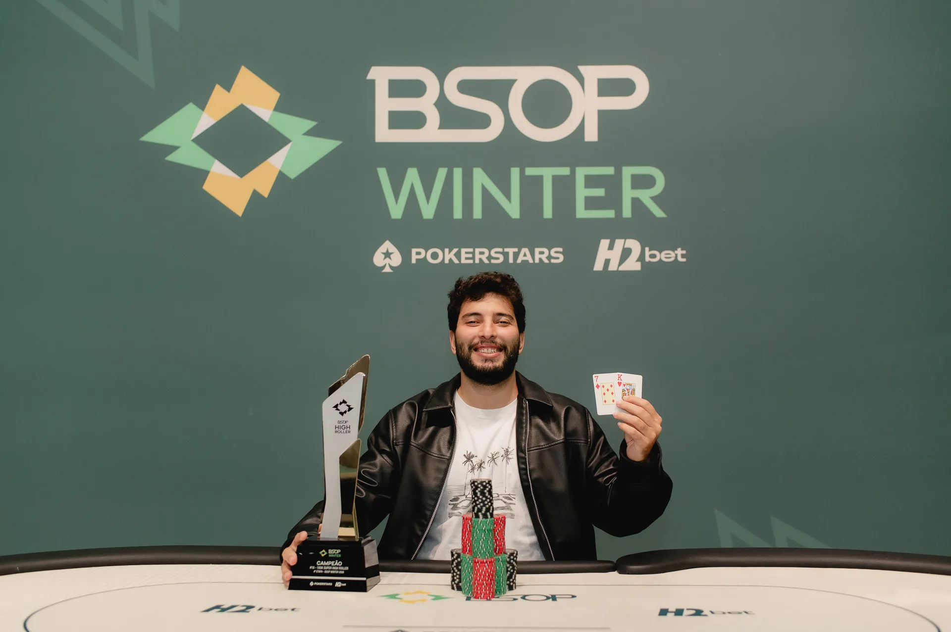 Iago Botelho poses with the BSOP Winter Super High Roller trophy and a pile of Brazilian reais chips
