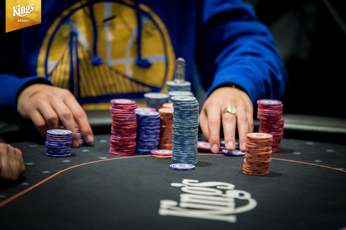 Players at a poker table during a tournament, with chip stacks visible.