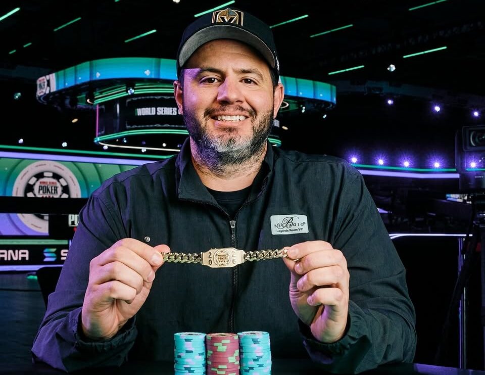 A poker player at a final table, holding cards and chips, with other players and dealers visible.